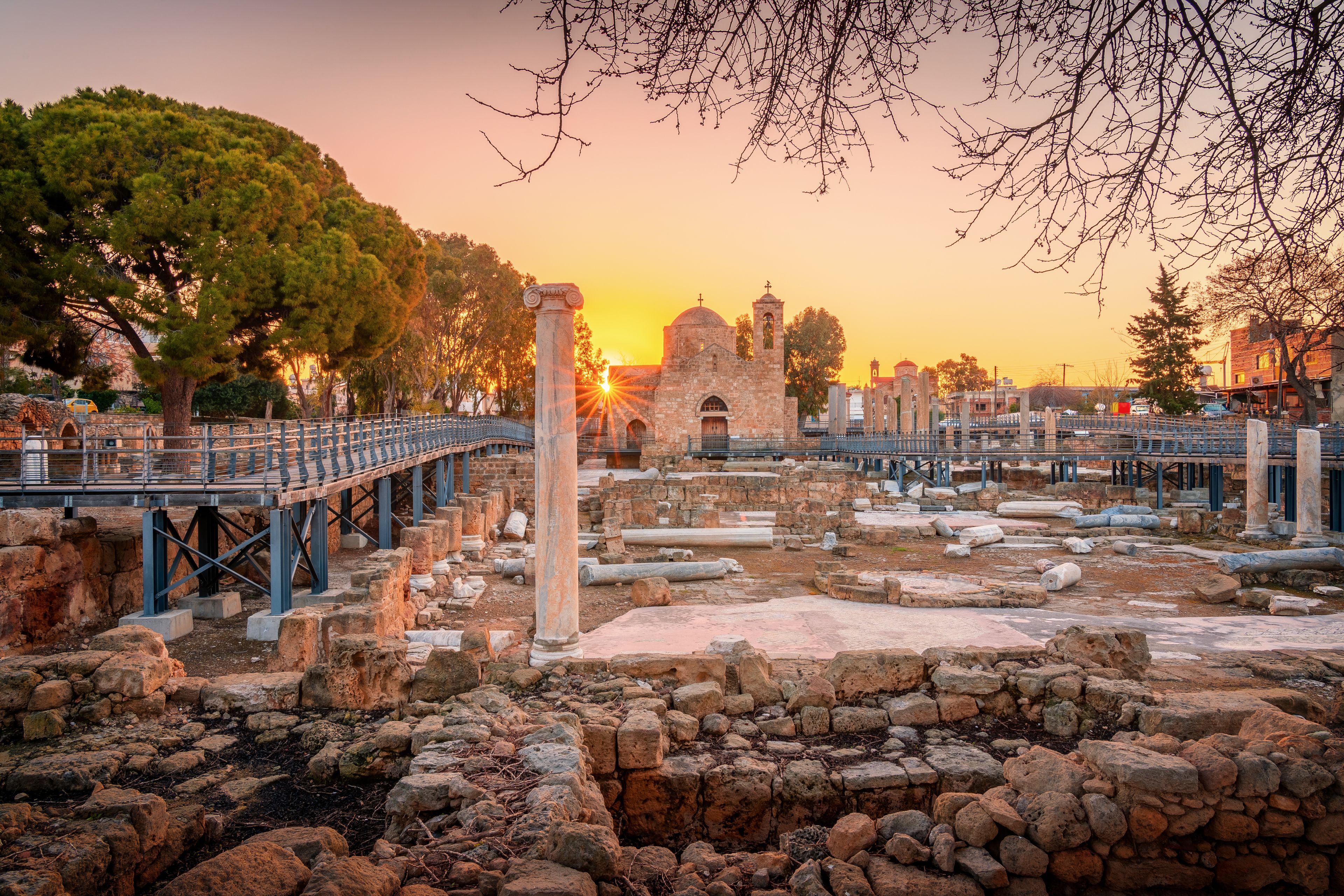 Ancient ruins with stone columns and a bridge, set against a sunset sky.