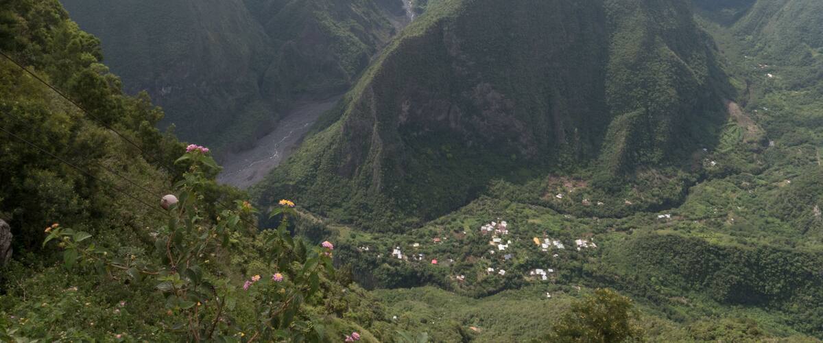 A lush valley with steep hills, a river, and scattered houses.