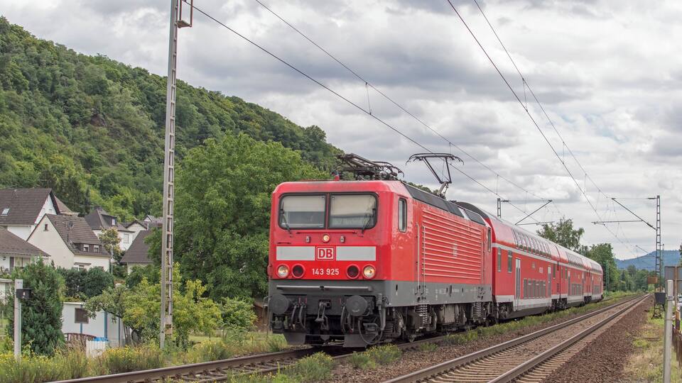 A red train on tracks with houses and a hill in the background.