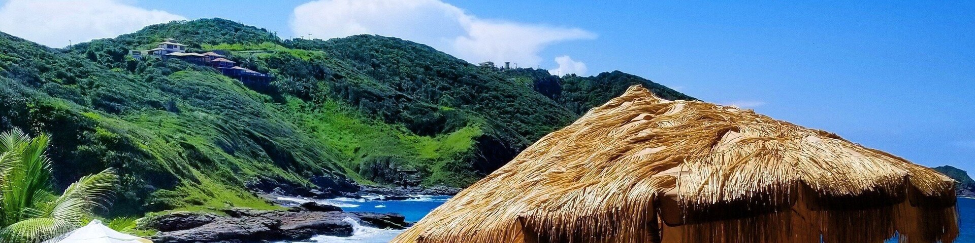 Uma praia com guarda-sóis de palha, cadeiras de espreguiçadeira e vista para o oceano.