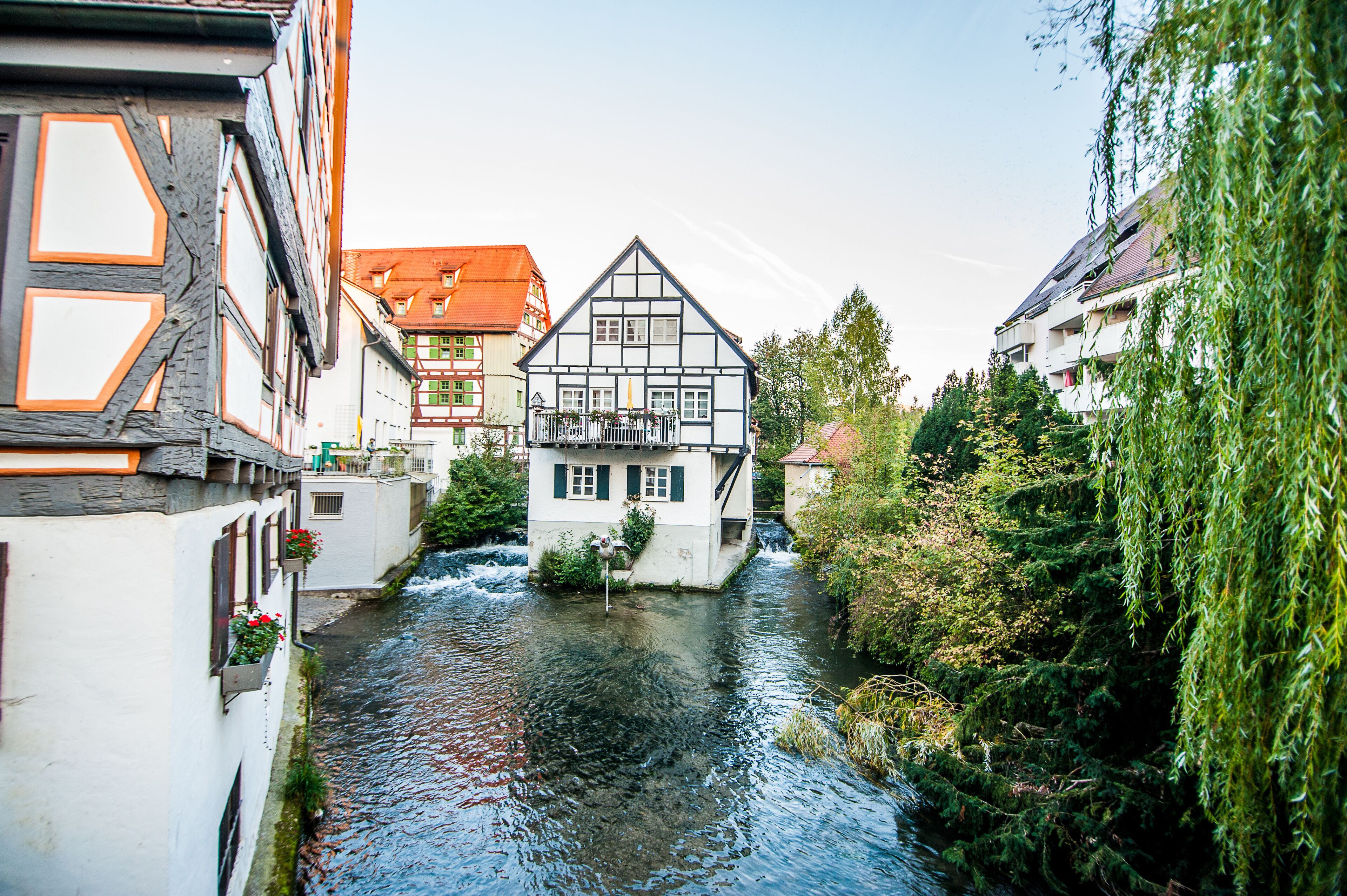 A narrow river in a town with traditional half-timbered houses and a modern building with a sloped roof.