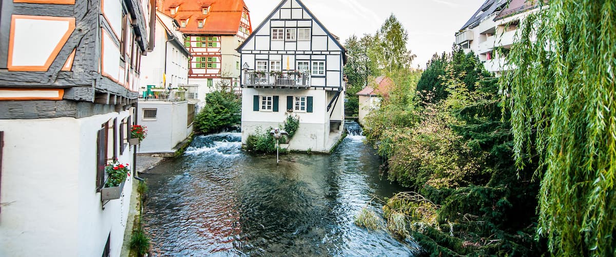 A narrow river in a town with traditional half-timbered houses and a modern building with a sloped roof.