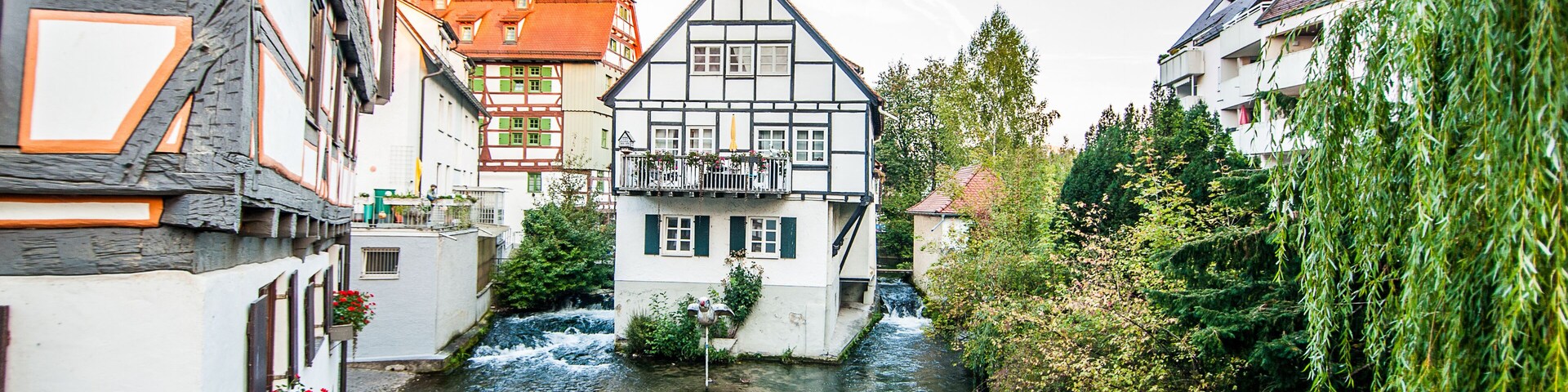 A narrow river in a town with traditional half-timbered houses and a modern building with a sloped roof.