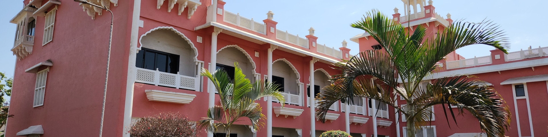 Un edificio rosa con balcones blancos y un jardín delantero.