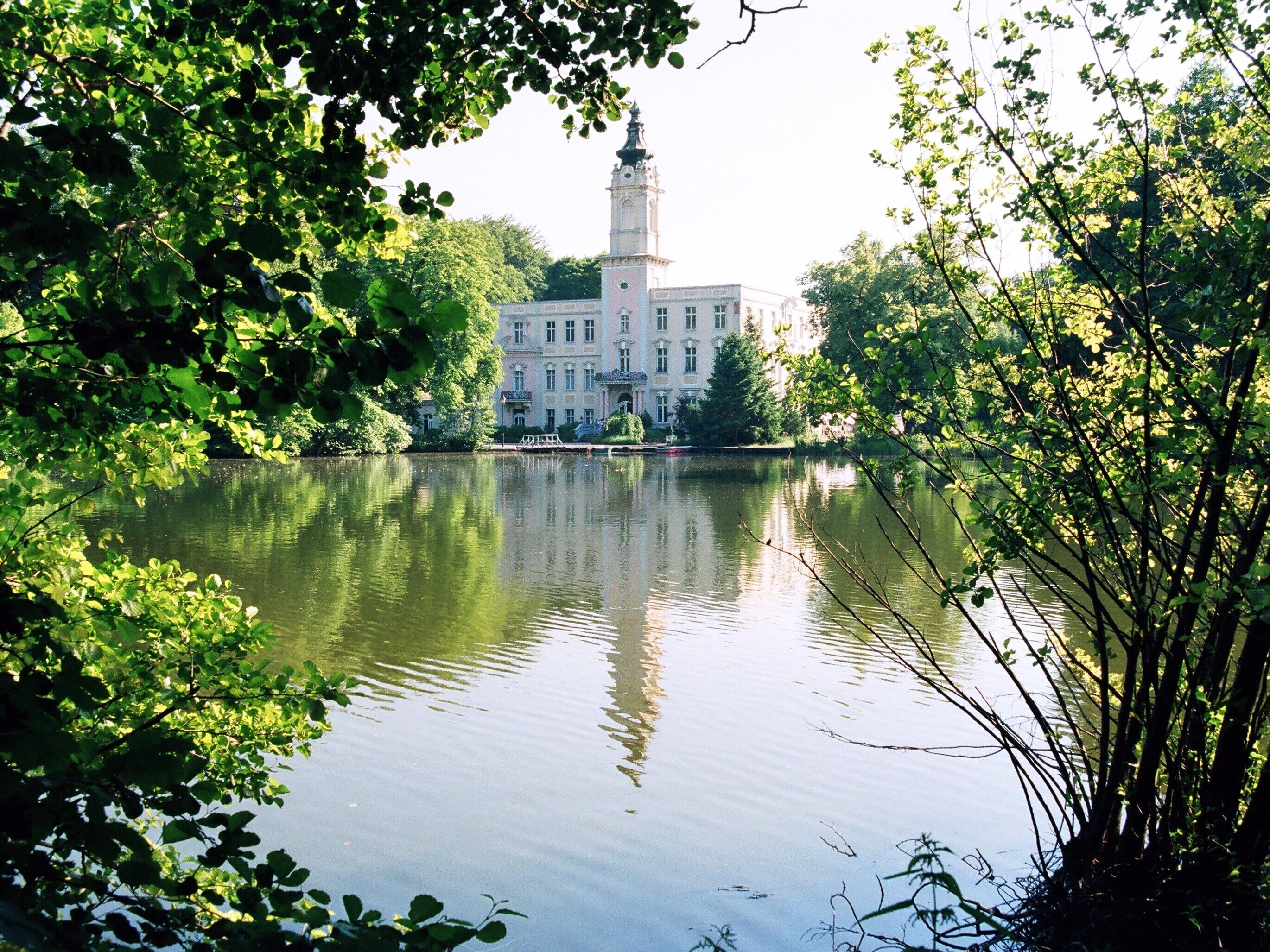A calm lake with a reflection of a historic building and surrounding greenery.