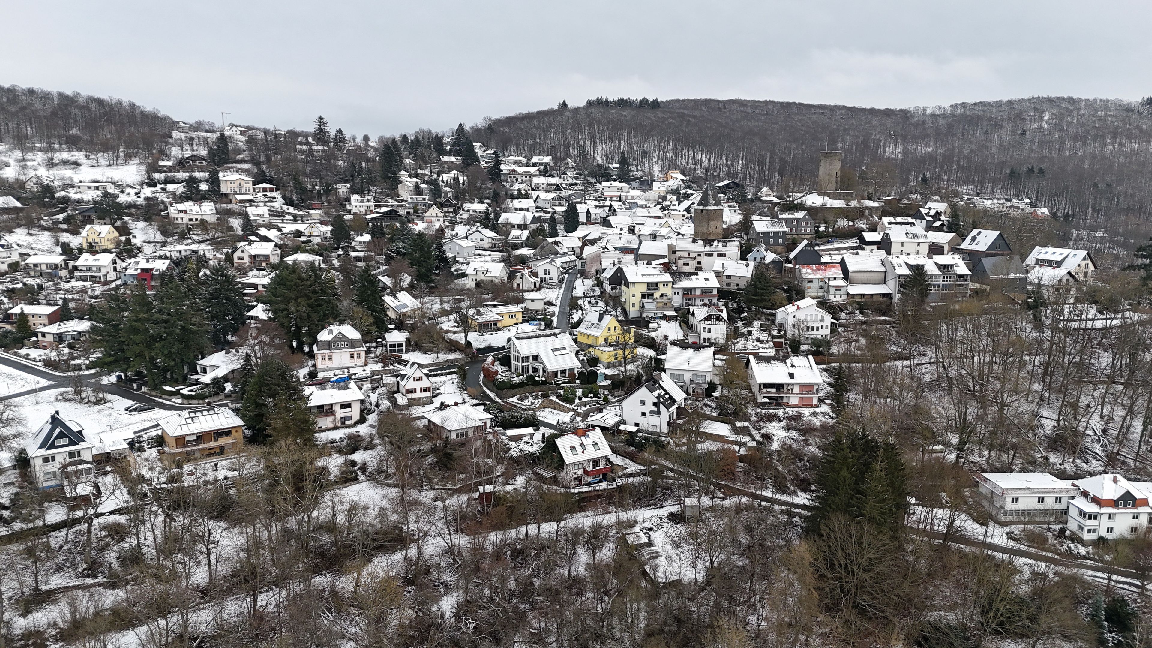 A snow-covered village with houses, a church, and a castle on a hill.