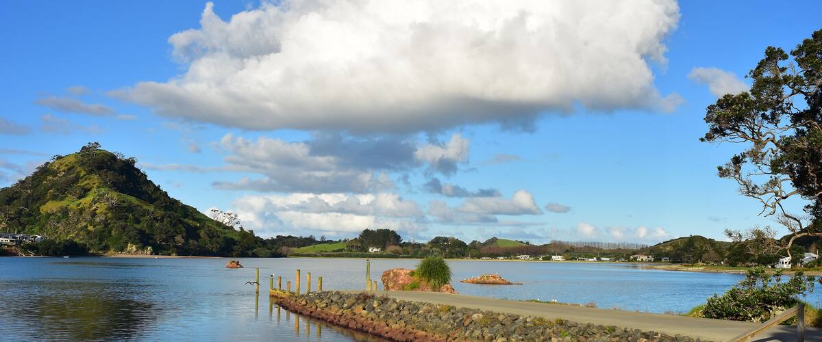 A calm lake with a wooden dock, a stone wall, and a hill with trees in the background.