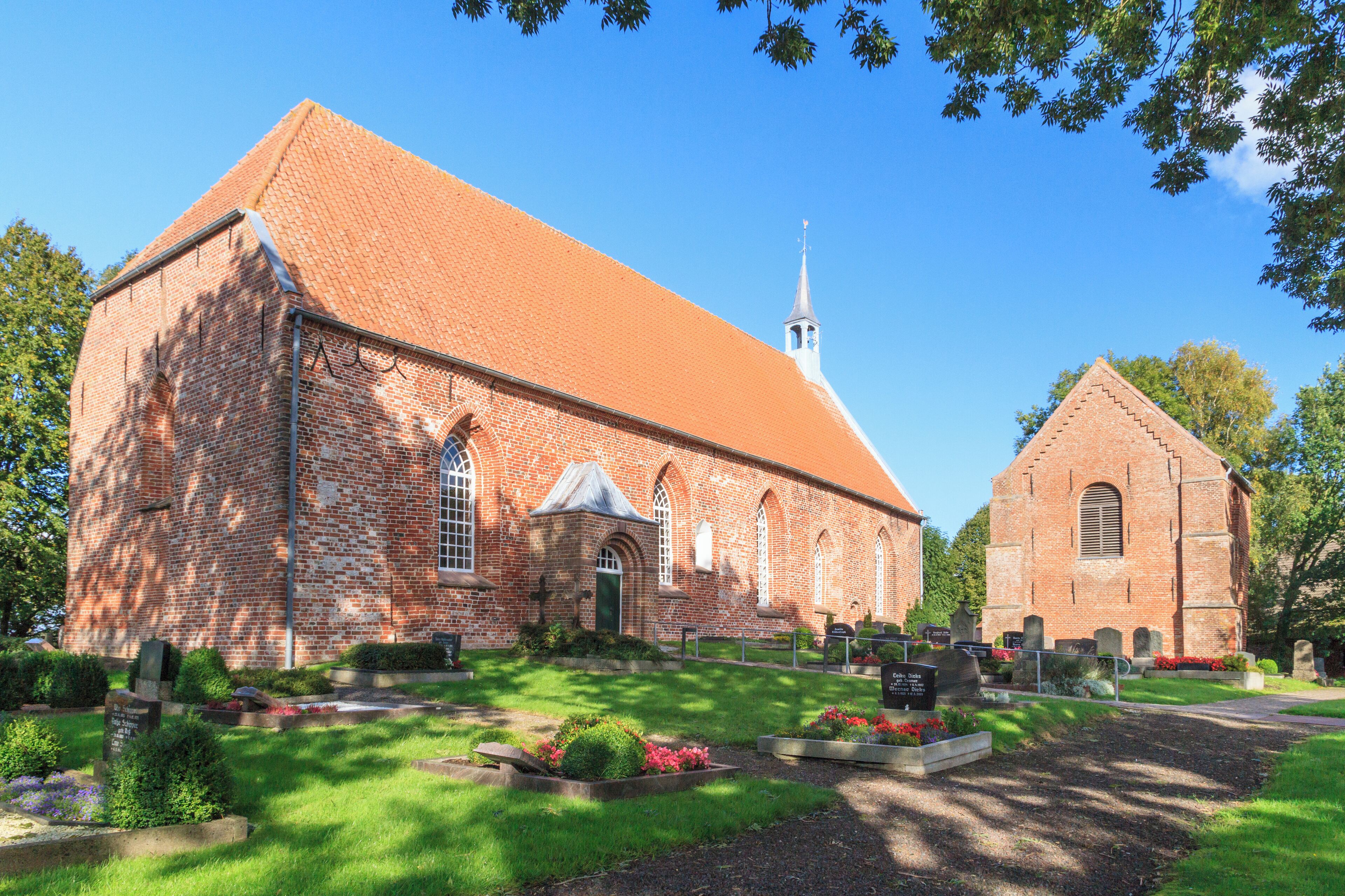 A large brick church with a steeple, surrounded by well-maintained gardens and a cemetery.