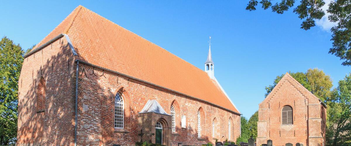 A large brick church with a steeple, surrounded by well-maintained gardens and a cemetery.