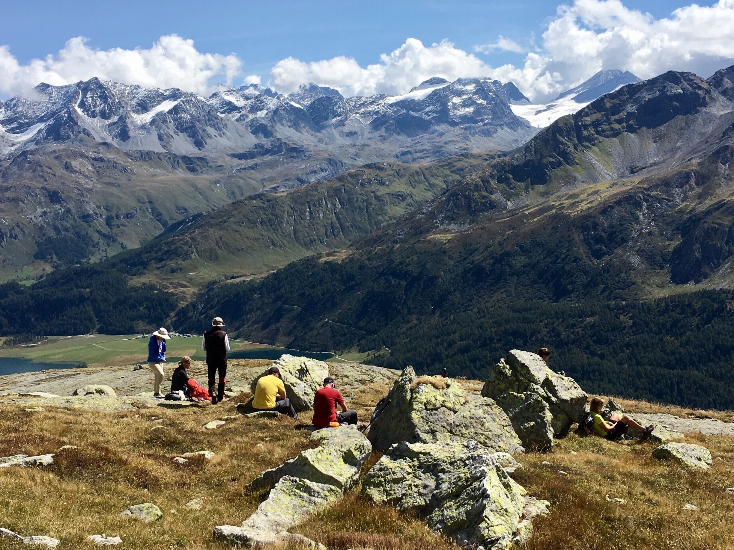 A group of hikers on a mountain trail with snow-capped peaks in the background.
