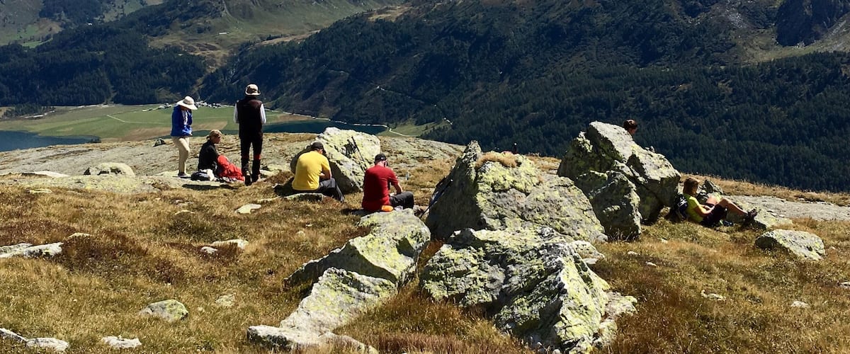 A group of hikers on a mountain trail with snow-capped peaks in the background.