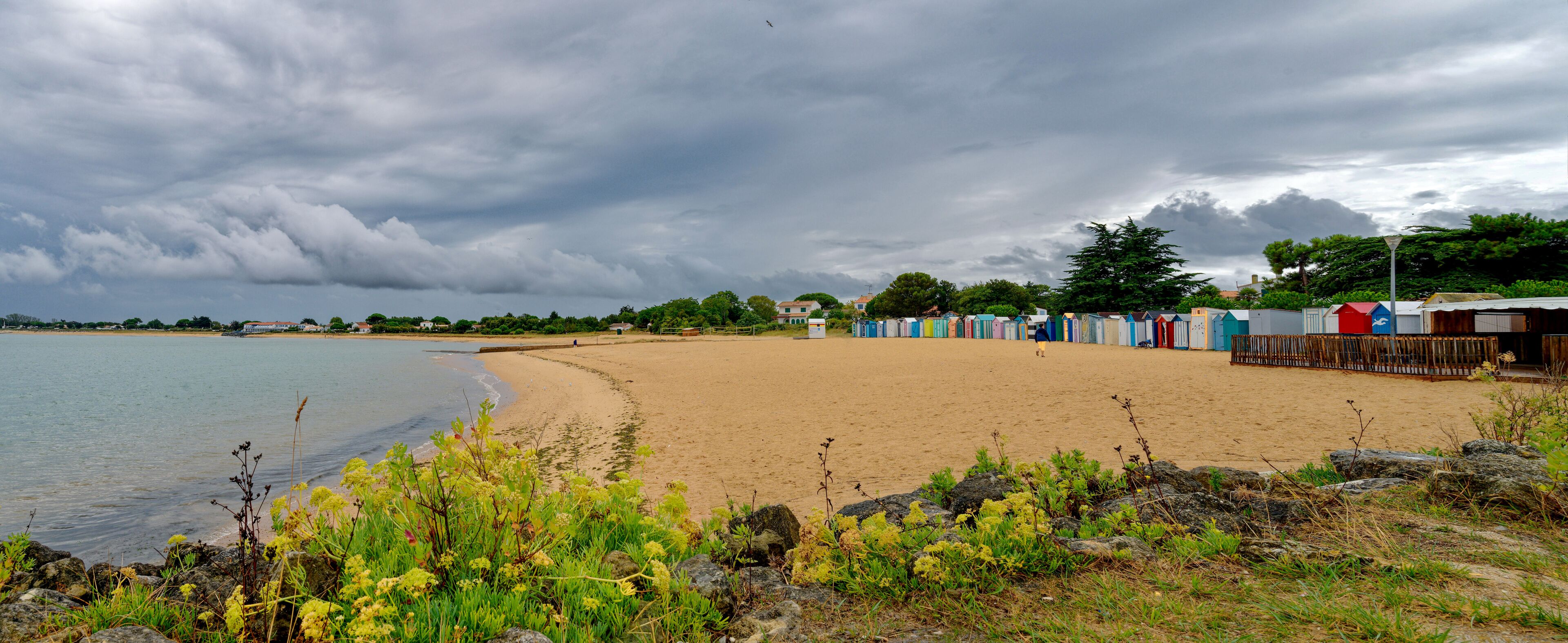 A beach with colorful beach huts, a sandy shore, and a cloudy sky.