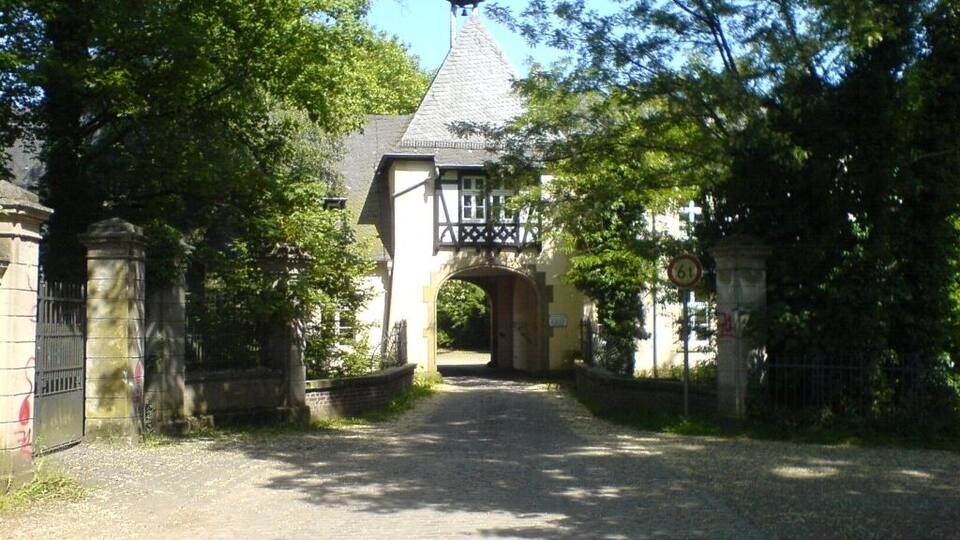 A narrow cobblestone path leading to a traditional building with a steeply pitched roof and a small tower.