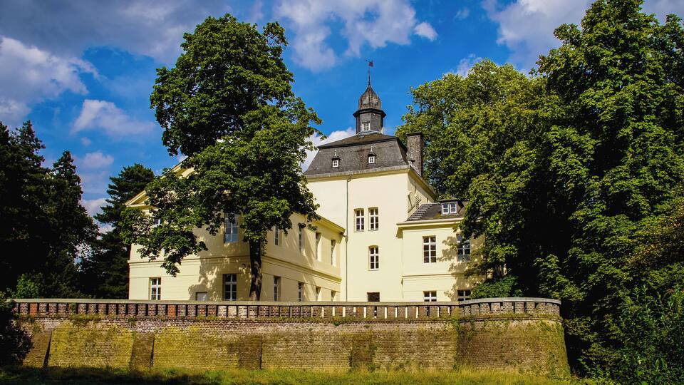 A large, historic building with a prominent tower and surrounded by lush greenery.