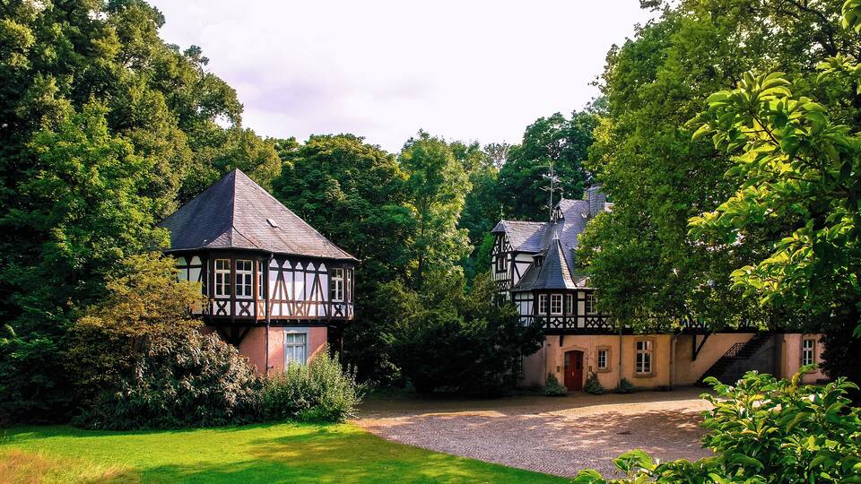 A Tudor-style house with a gravel driveway and lush greenery.