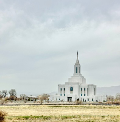A large white building with a tall spire, surrounded by open fields and sparse trees.