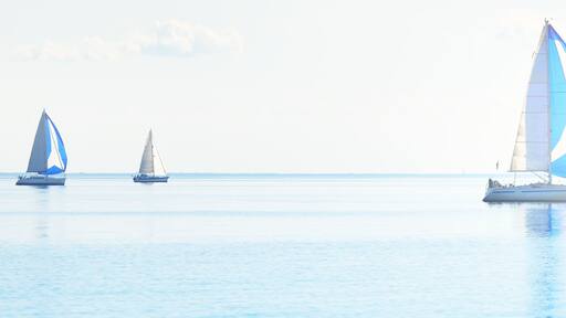 Drei Segelboote auf ruhigem Wasser unter blauem Himmel.