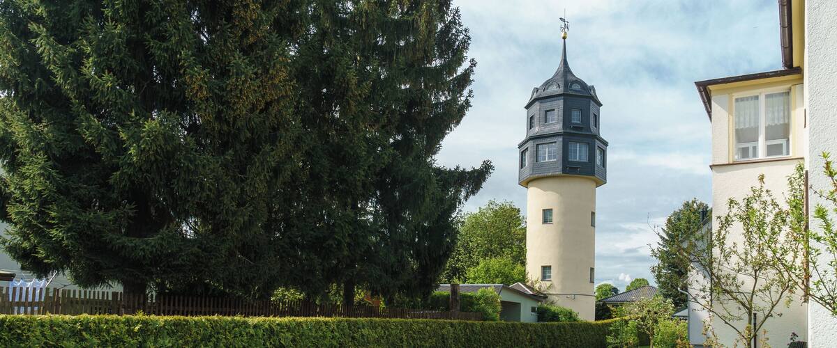 A tower with a weather vane, a hedge, and a brick pathway.