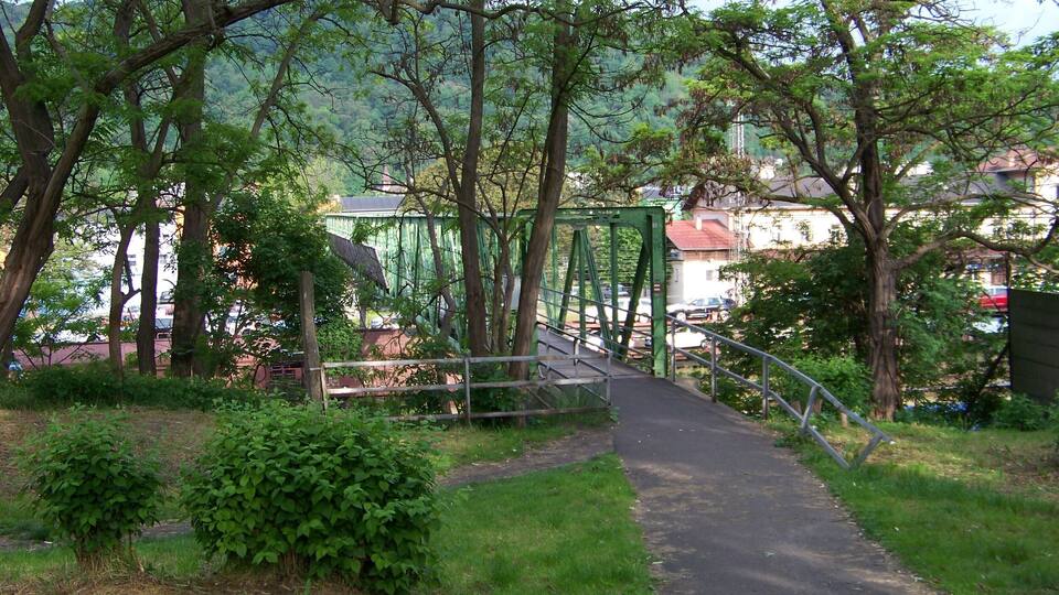 A green metal bridge over a paved path surrounded by trees and grass.