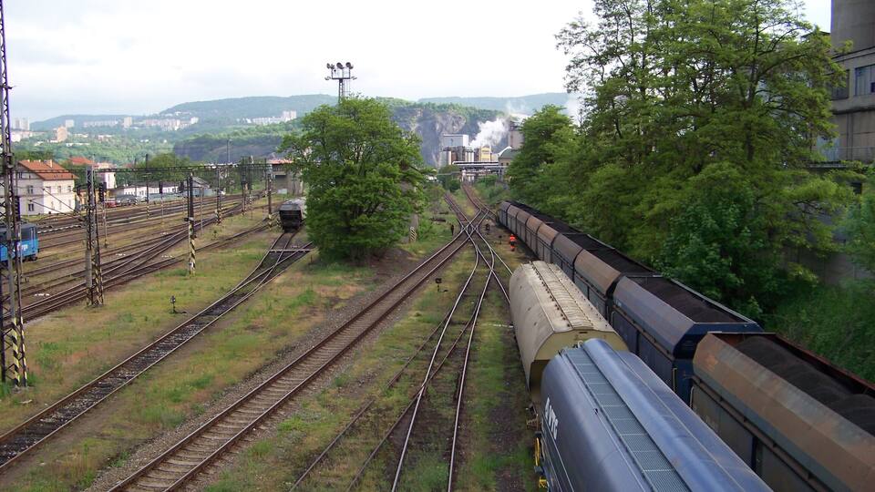 A railway yard with multiple tracks, a train, and industrial buildings in the background.