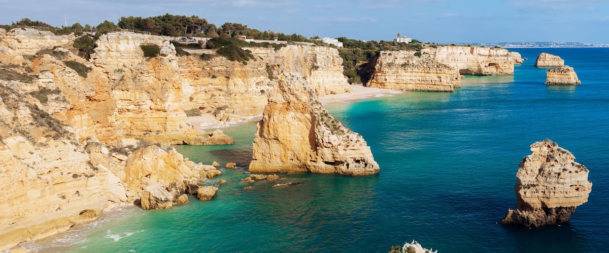 A coastal landscape with white cliffs, clear turquoise waters, and a sandy beach.