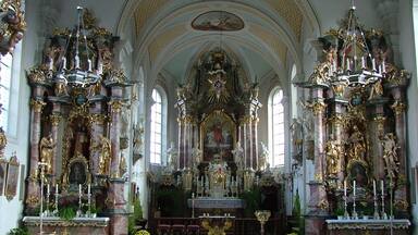 An ornate church interior with high ceilings, detailed altars, and religious statues.