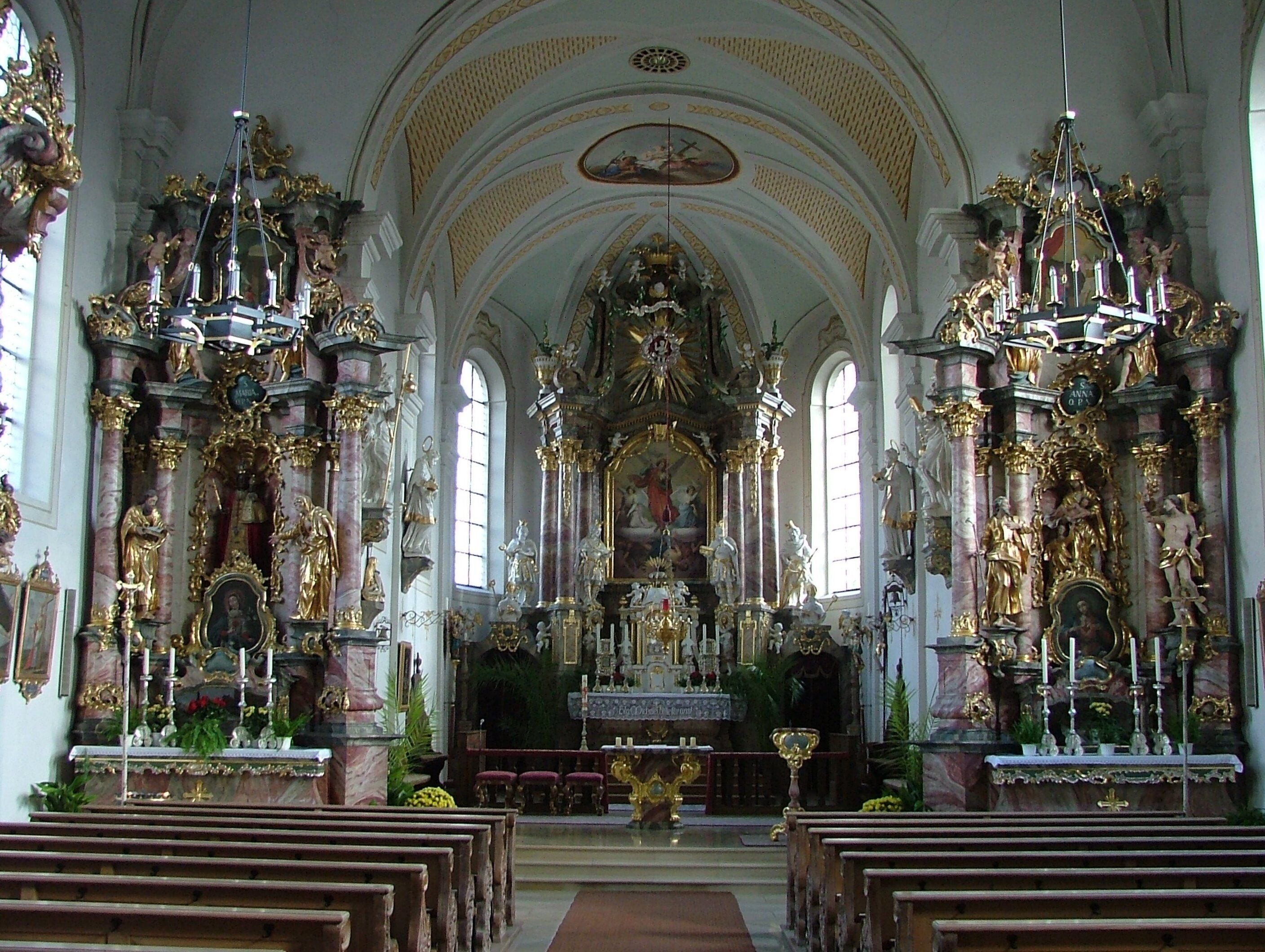 An ornate church interior with high ceilings, detailed altars, and religious statues.
