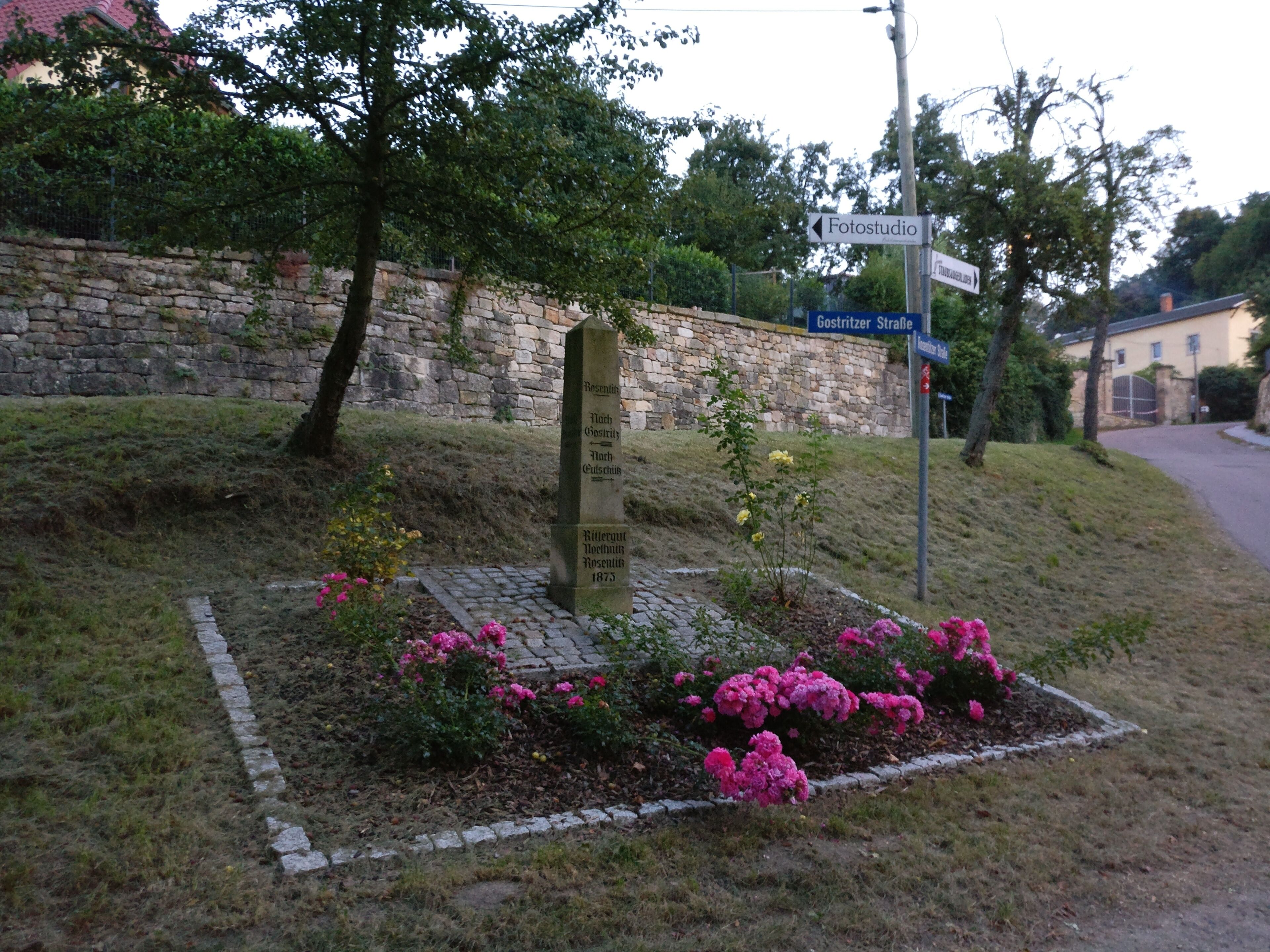 A stone monument with inscriptions surrounded by flowers and a stone wall.