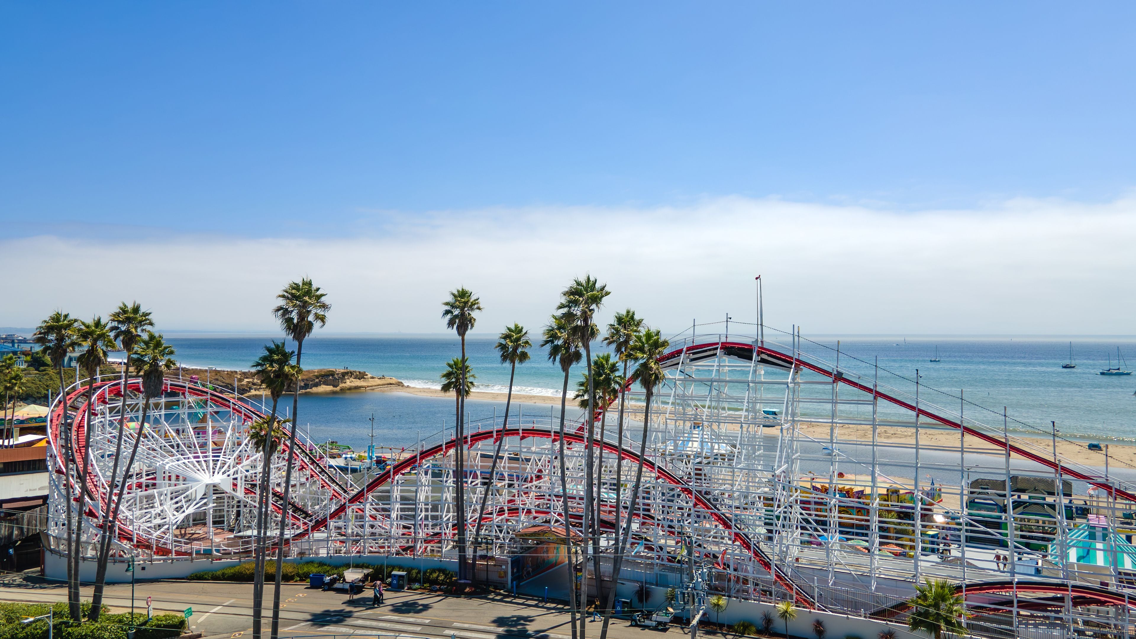 A roller coaster at an amusement park with a beach and ocean in the background.
