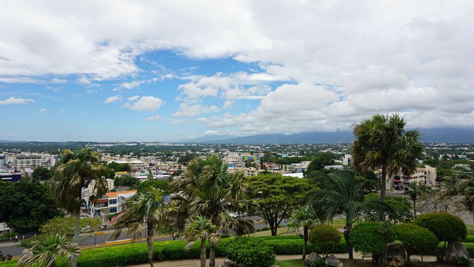 A cityscape with palm trees, buildings, and mountains in the background.