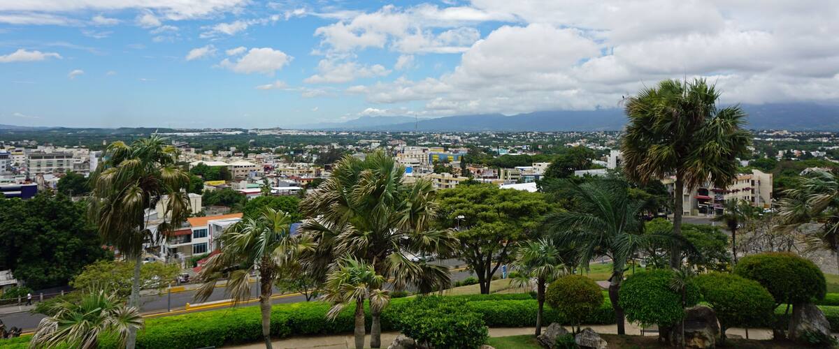 A cityscape with palm trees, buildings, and mountains in the background.