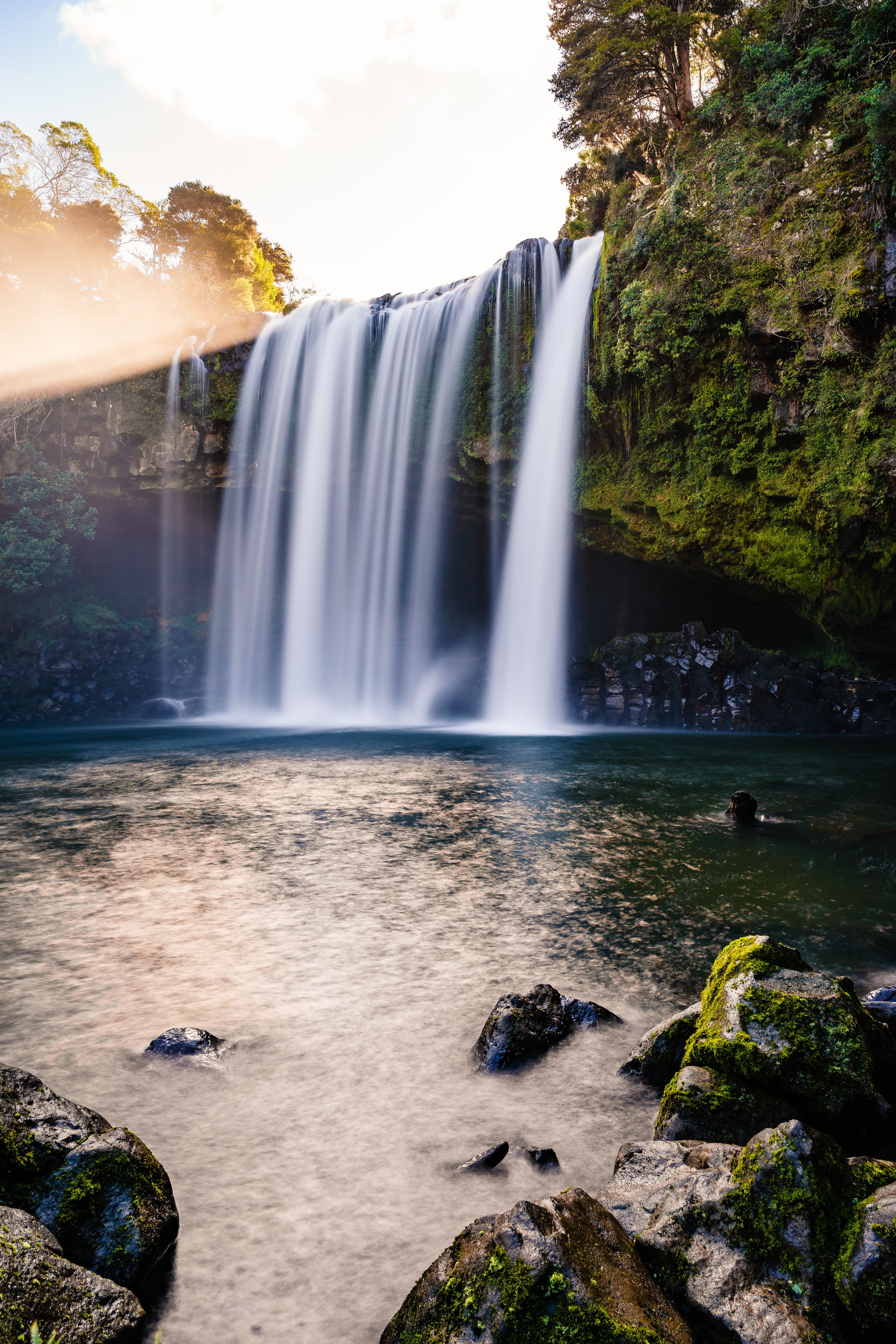 A waterfall cascading over moss-covered rocks into a calm river.