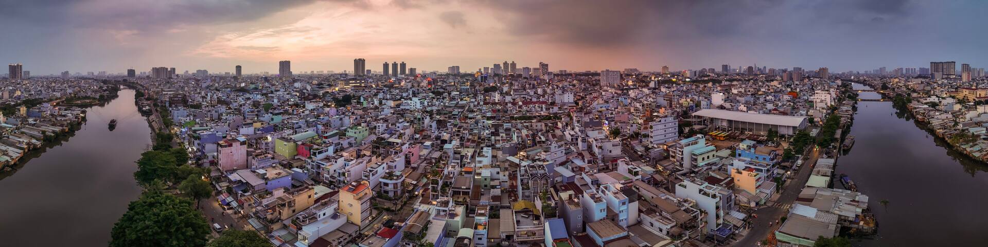 A densely populated urban area with a river running through it, surrounded by various buildings and a cloudy sky.