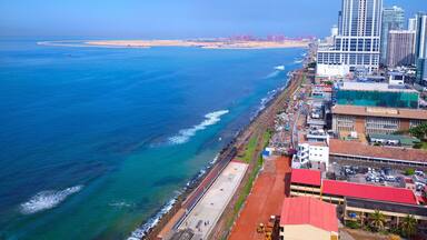 A coastal cityscape with a prominent skyscraper, a beach, and a port area.