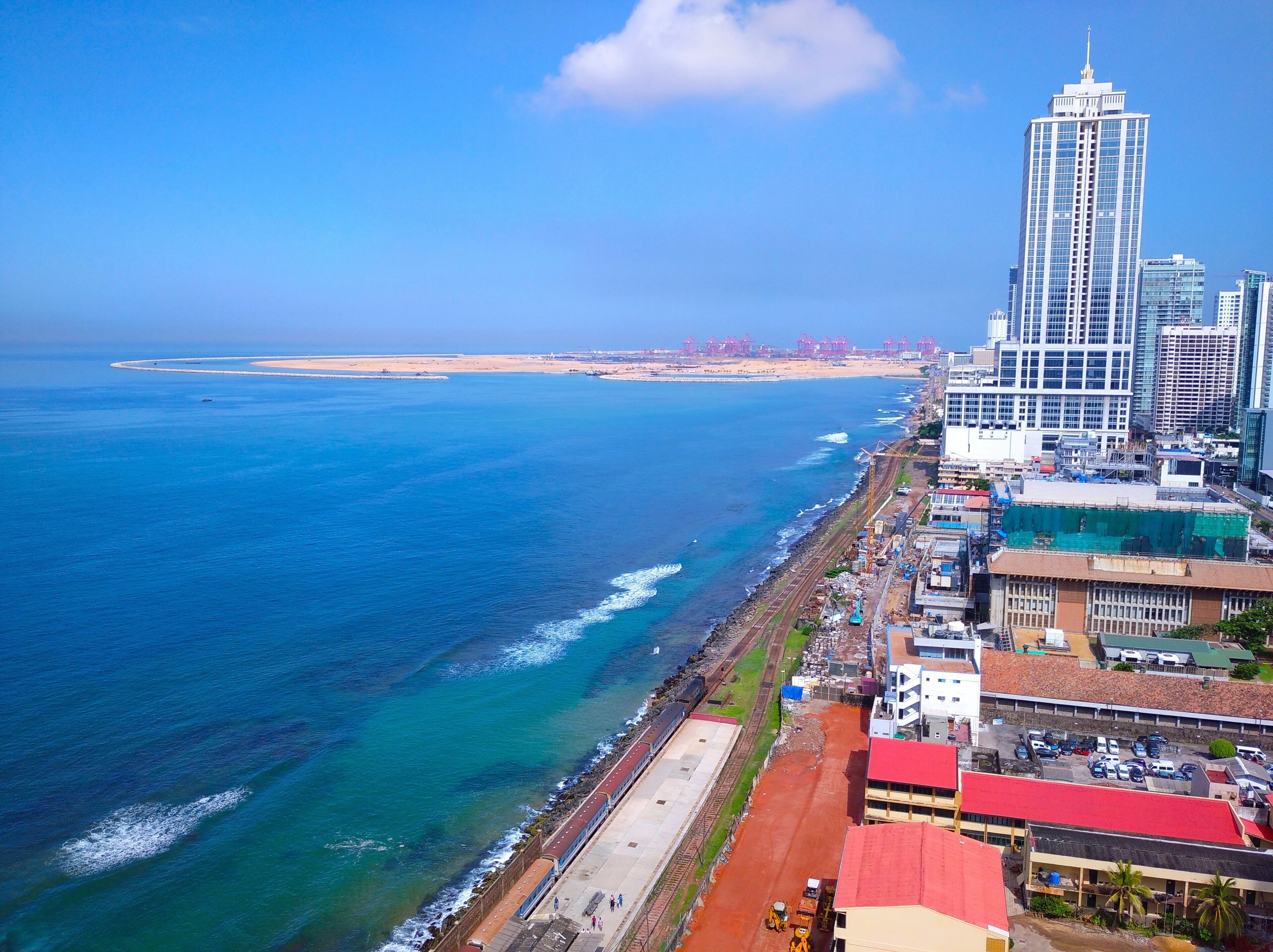 A coastal cityscape with a prominent skyscraper, a beach, and a port area.