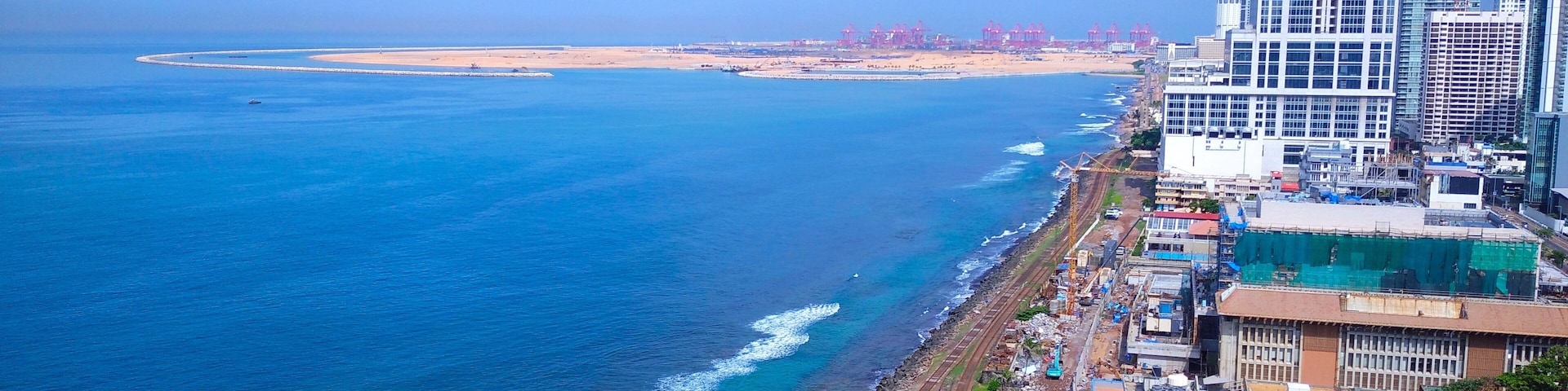 A coastal cityscape with a prominent skyscraper, a beach, and a port area.
