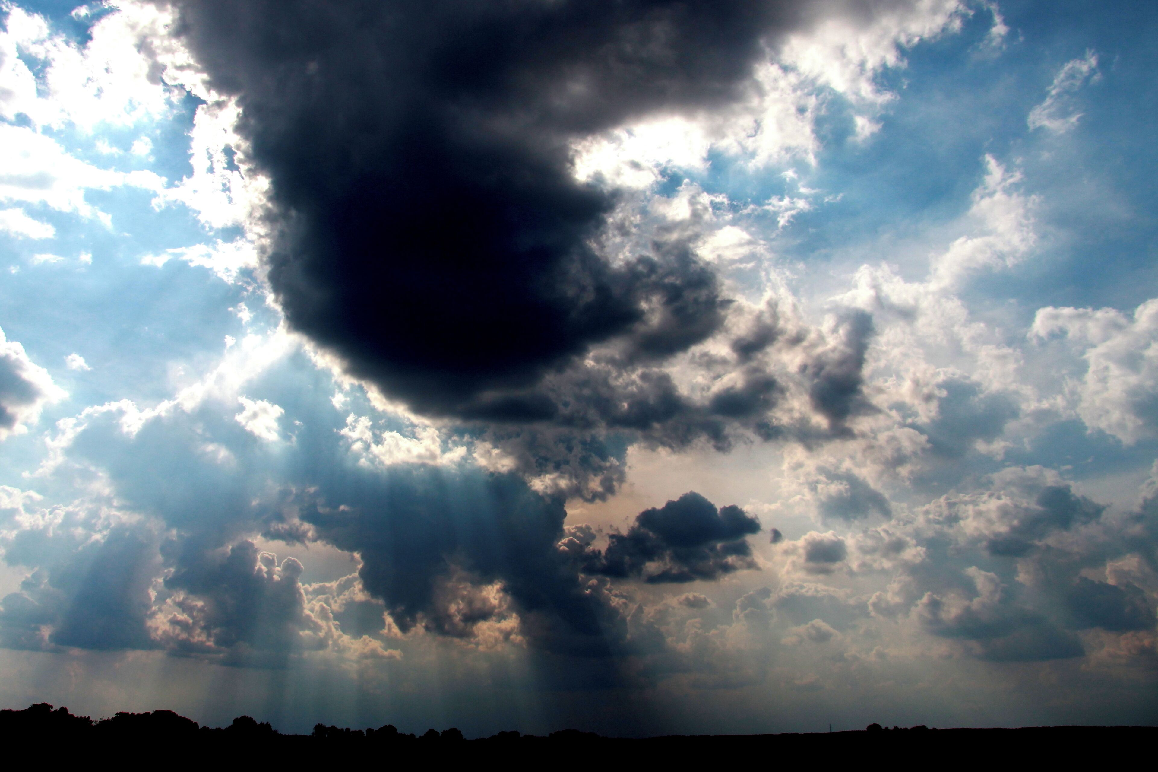 A dramatic sky with a large dark cloud formation and rays of sunlight breaking through.