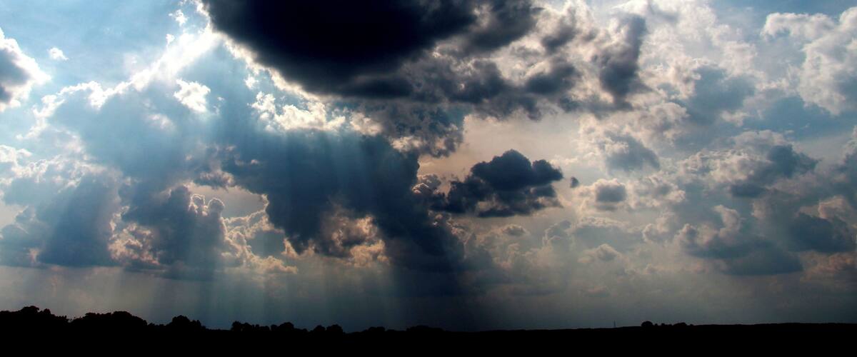 A dramatic sky with a large dark cloud formation and rays of sunlight breaking through.