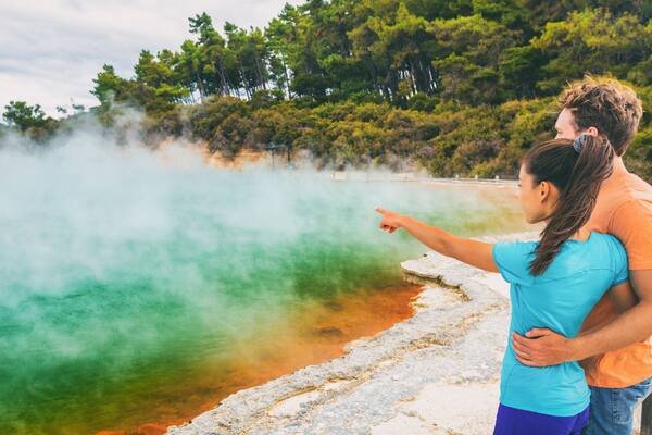 New Zealand travel tourists couple at Champagne pool at Wai-O-Tapu pools Sacred Waters. Tourist attraction in Waiotapu, Rotorua, north island. Panoramic banner, Okataina Volcanic Centre, Taupo.