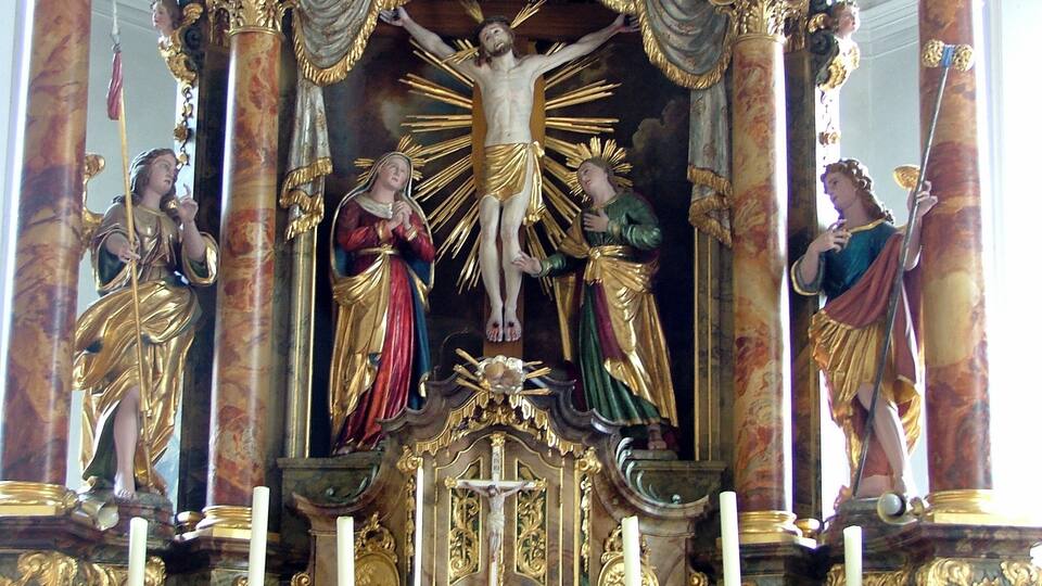 A religious statue with a central figure of Jesus on the cross, flanked by two angels, set within an ornate, gilded structure.