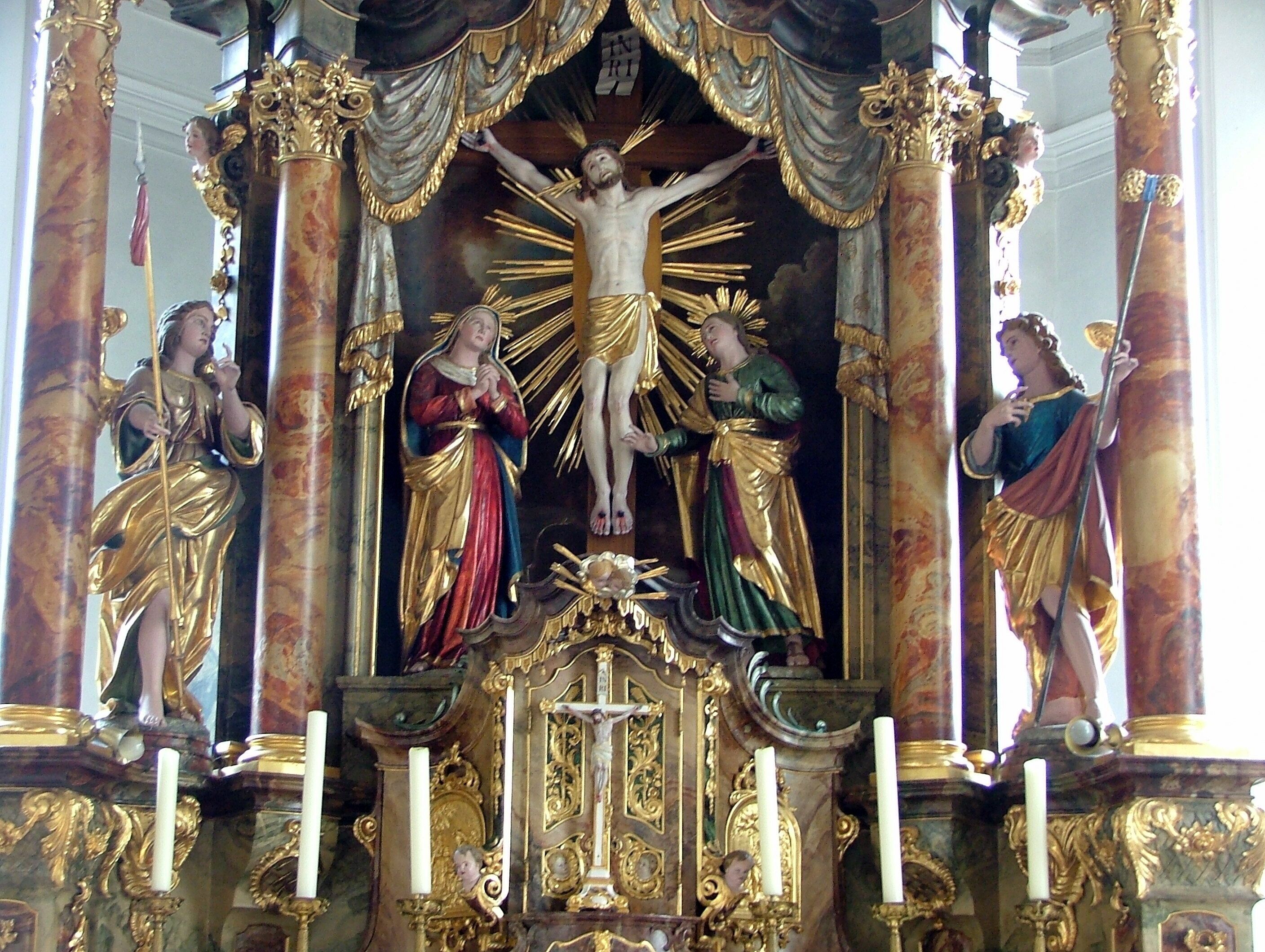 A religious statue with a central figure of Jesus on the cross, flanked by two angels, set within an ornate, gilded structure.