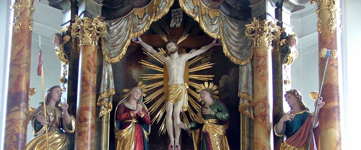 A religious statue with a central figure of Jesus on the cross, flanked by two angels, set within an ornate, gilded structure.