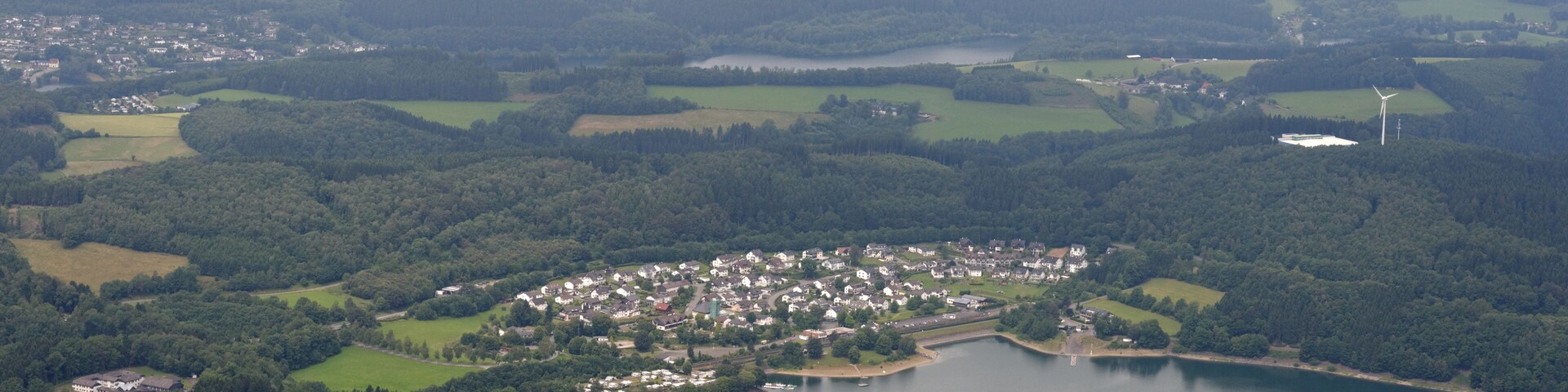 A coastal town surrounded by a lake, with wind turbines in the distance.