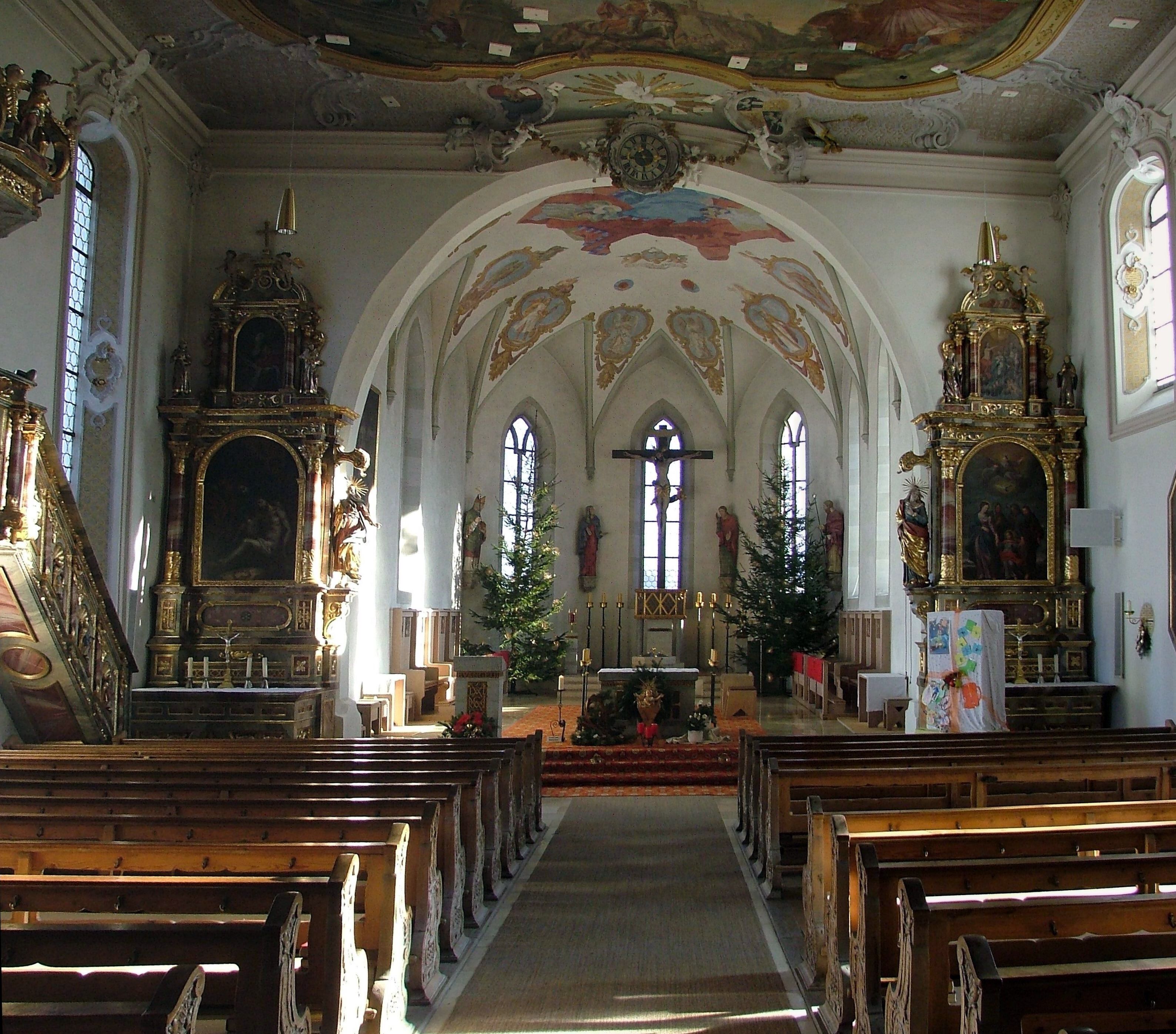 An ornate church interior with wooden pews, a crucifix, and a Christmas tree.
