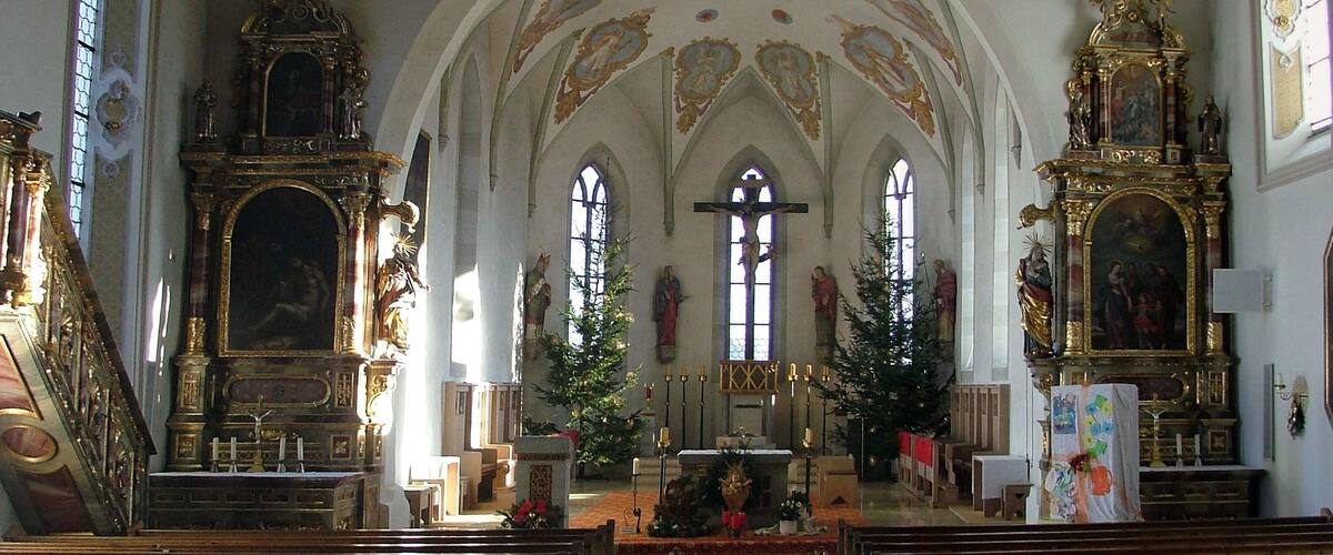 An ornate church interior with wooden pews, a crucifix, and a Christmas tree.