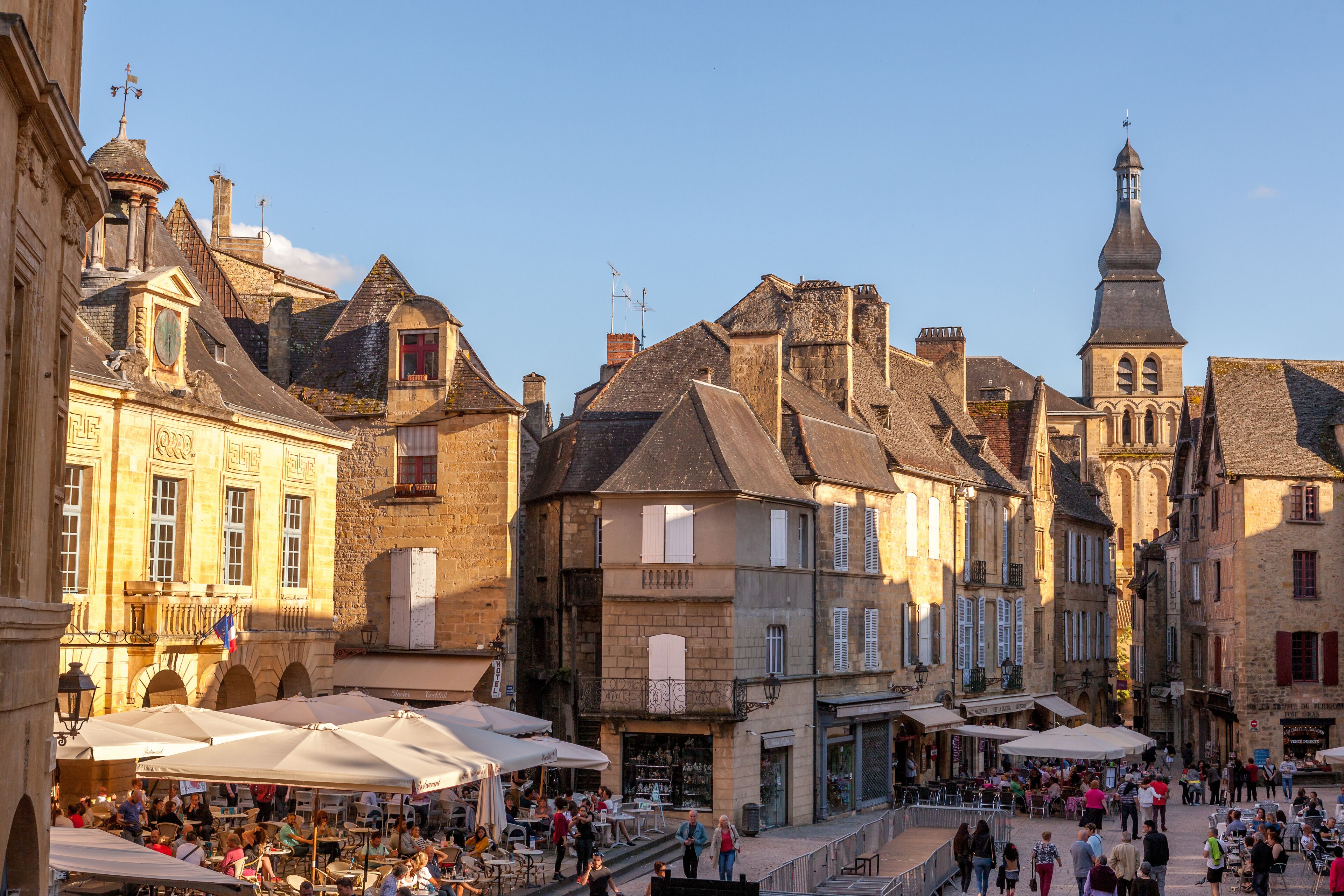 A bustling European town square with historic buildings, outdoor cafes, and a prominent church tower.