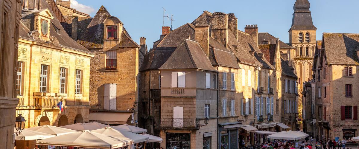 A bustling European town square with historic buildings, outdoor cafes, and a prominent church tower.