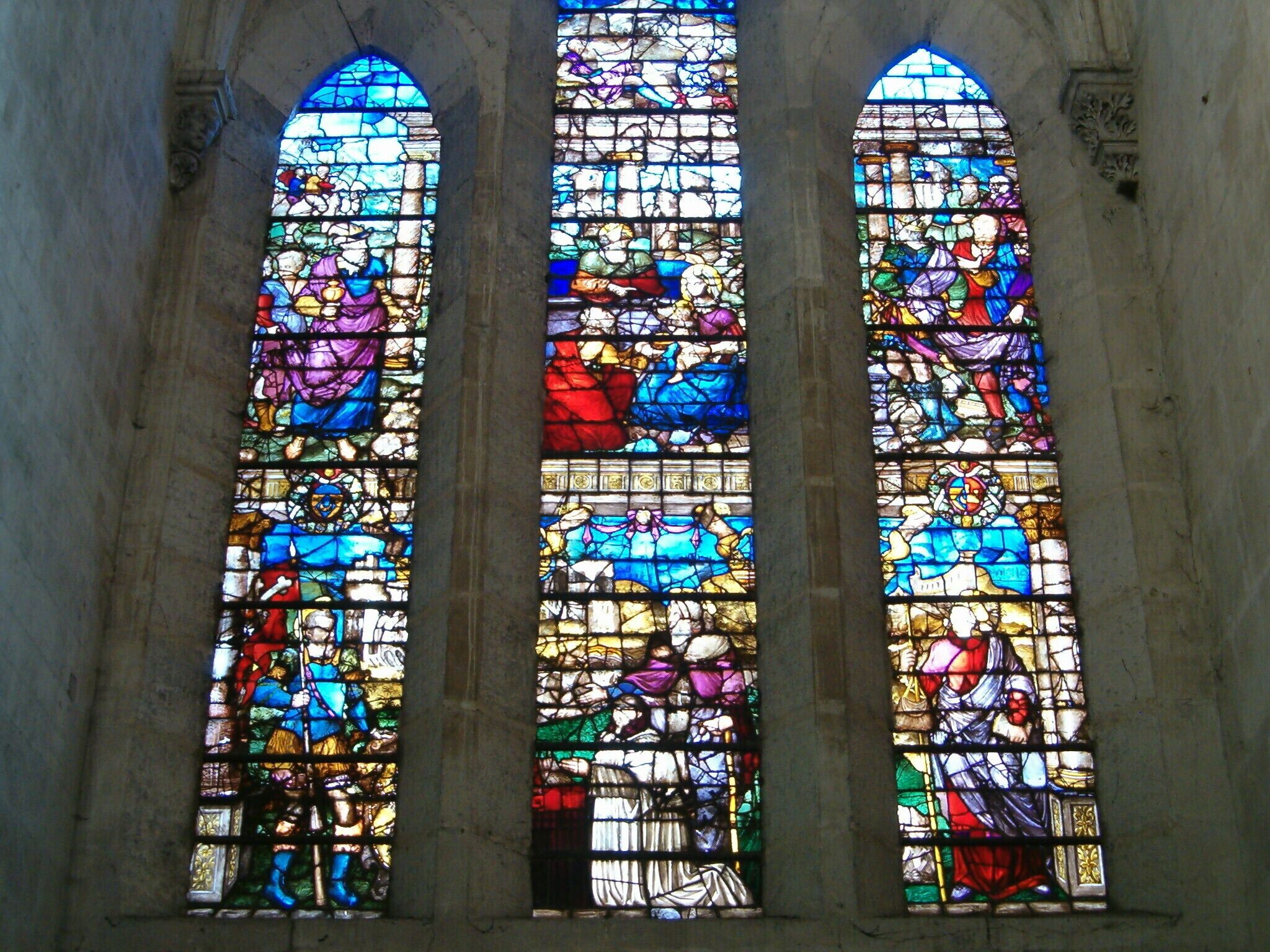 Three stained glass windows with religious scenes.