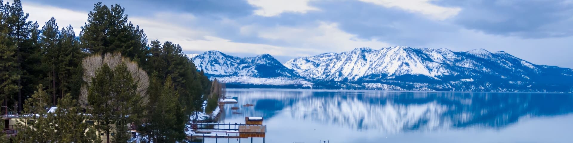 Calm mirror Lake Tahoe, pier and mountains with snow. Tahoe Keys, South Lake Tahoe, California, United States of America.