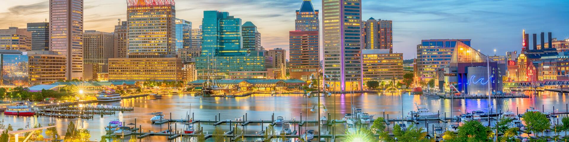 A city skyline with modern buildings, a marina with boats, and a river reflecting the lights.